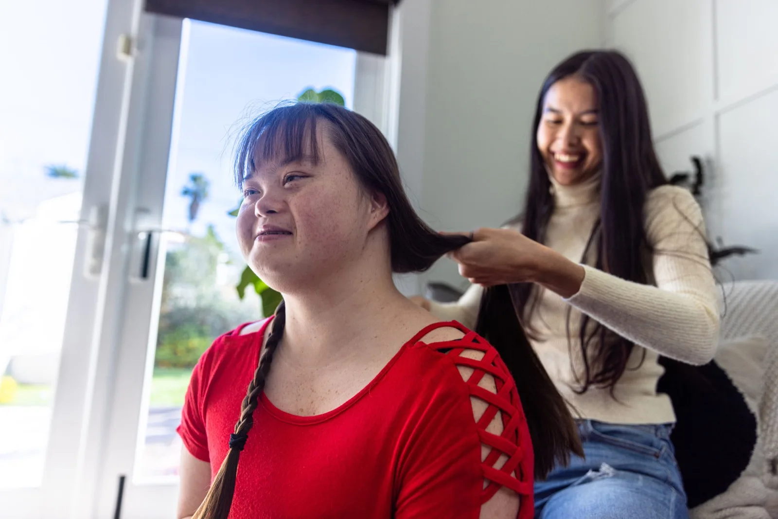 A support worker braiding a young woman's hair at home