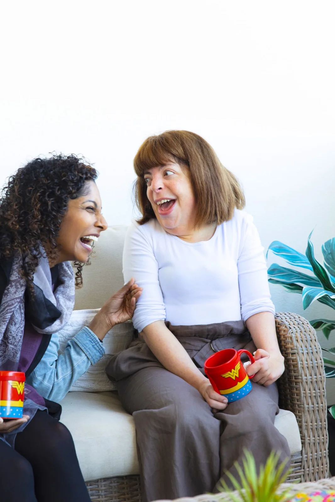 Two women laughing together over a cup of tea at home