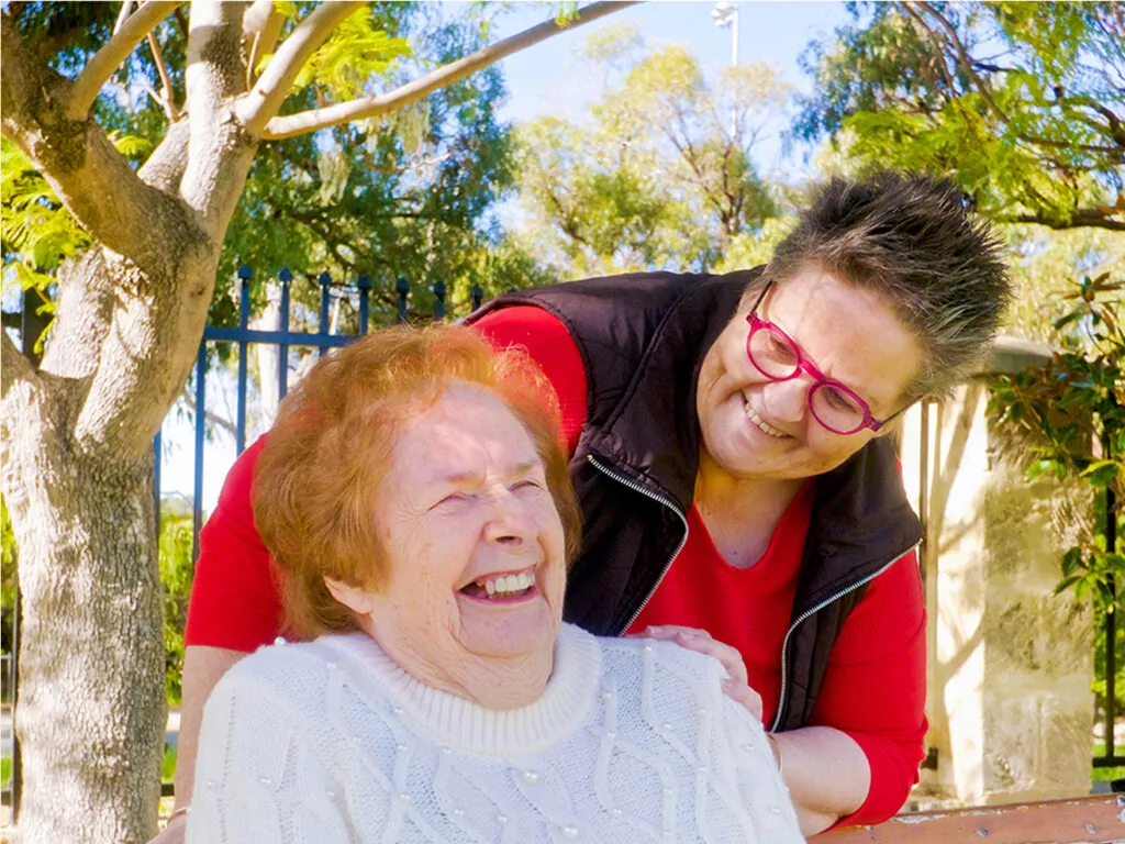 A support worker and an older woman laughing together outdoors
