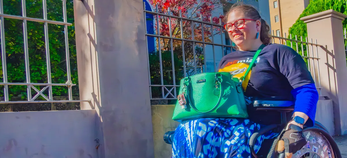 A woman smiling as she wheels along a sunny street